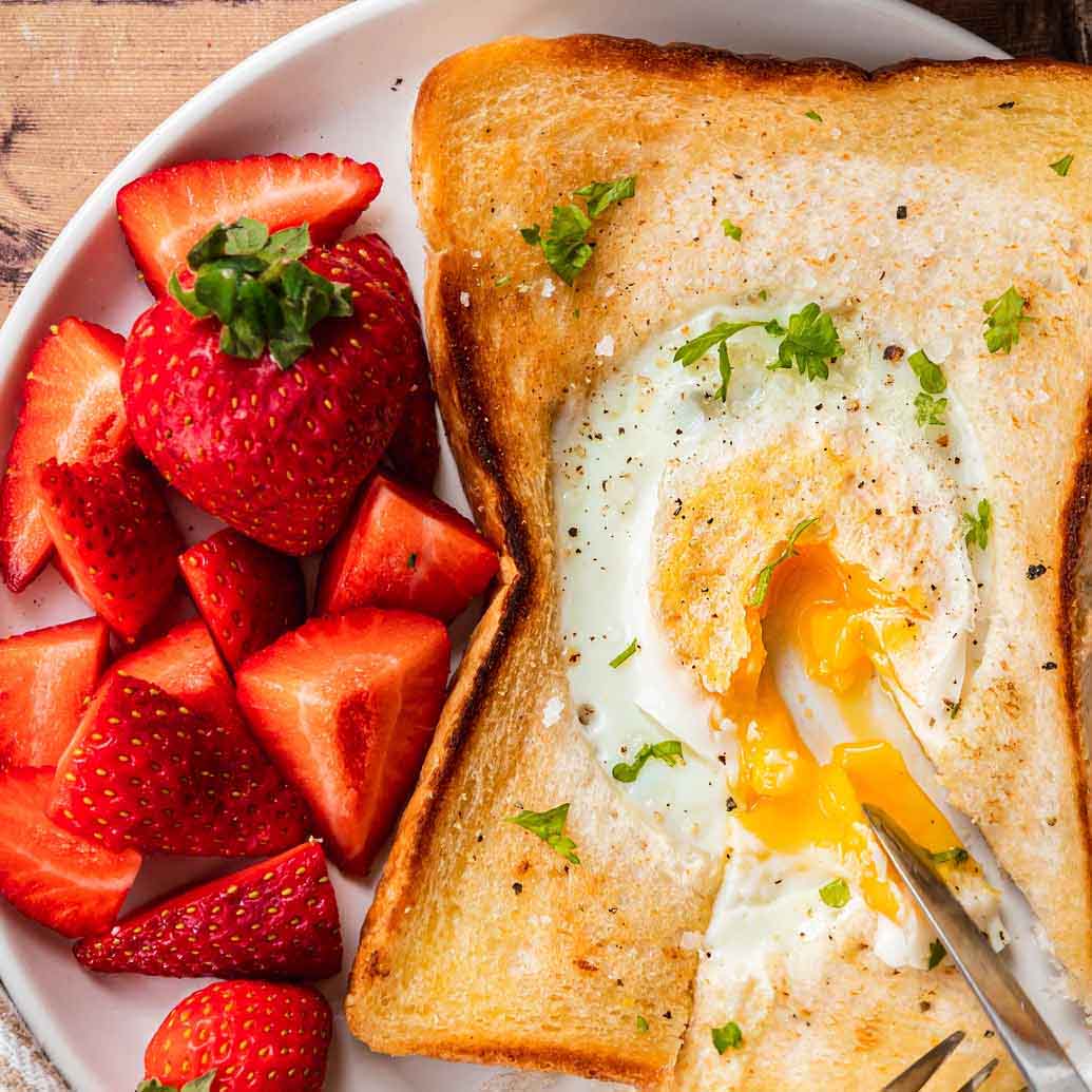 a piece of toast with a hole in the middle with a cooked egg in it and a side of strawberries