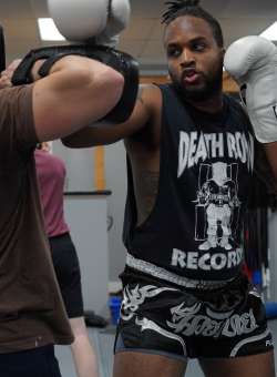 a black man with a high ponytail boxing wearing a t-shirt that says Death Row Records and fairtex muay thai shorts